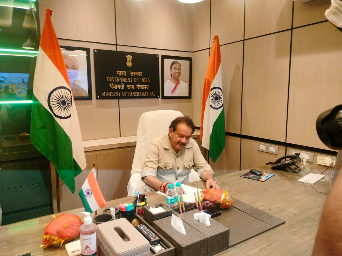 Satyapal Singh Baghel seated at a desk beneath a sign reading Government of India, Ministry of Panchayati Raj, between two national flags